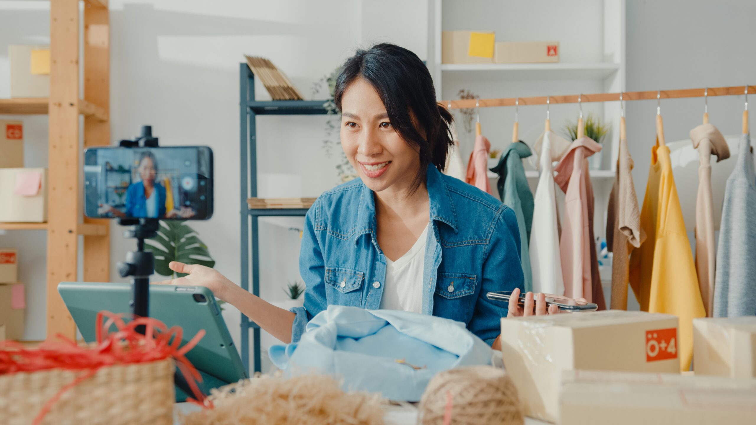 Woman facing and taking to recording camera, surrounded by clothing