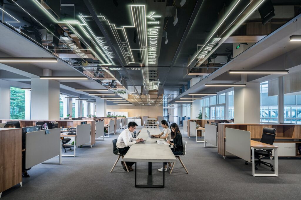 three people sitting at a table in the middle of a large modern office floor